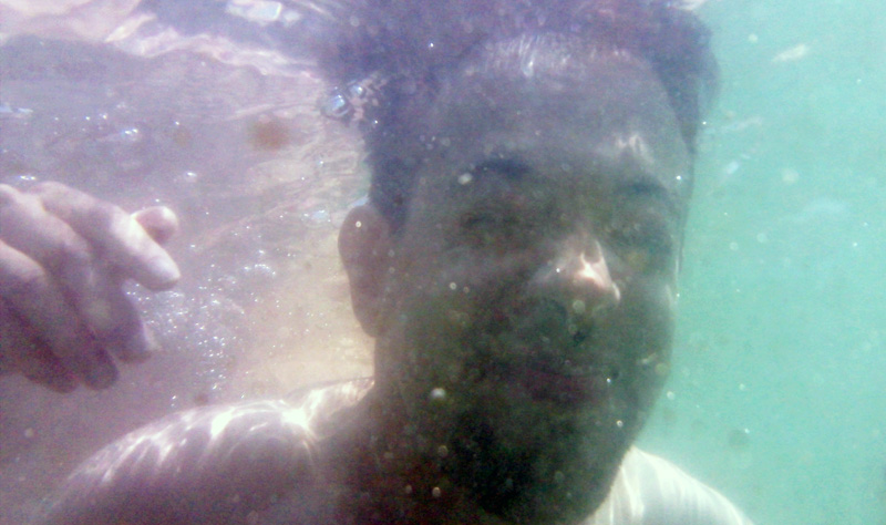 a person hovers just beneath the surface of turbid water, full of sediment and bubbles, eyes closed, entering a new element